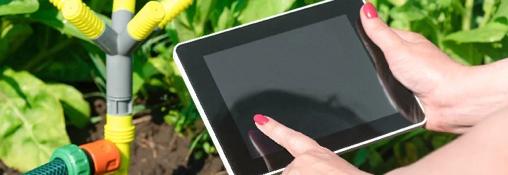 Person steuert mit einem Tablet die Bewässerung im Garten.